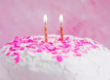 Geburtstagskuchen mit zwei Kerzen und rosa Dekoration vor hellem Hintergrund“