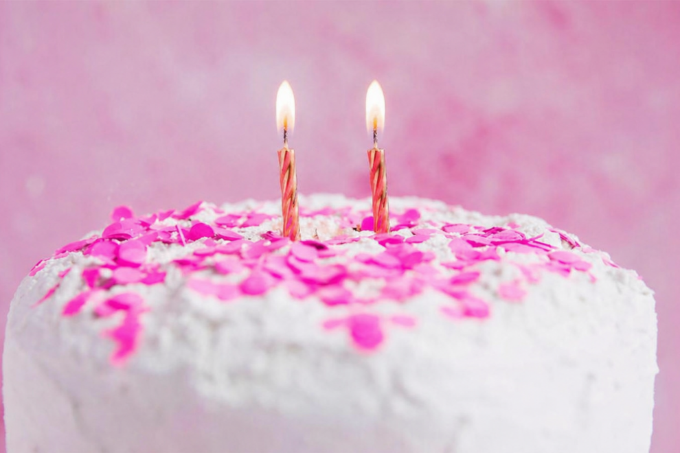 Geburtstagskuchen mit zwei Kerzen und rosa Dekoration vor hellem Hintergrund“