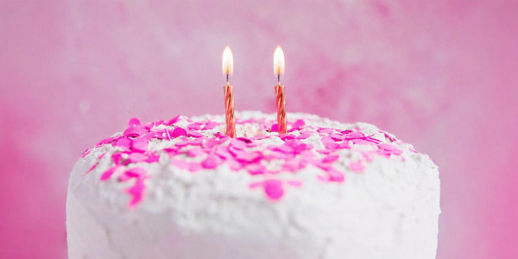 Geburtstagskuchen mit zwei Kerzen und rosa Dekoration vor hellem Hintergrund“